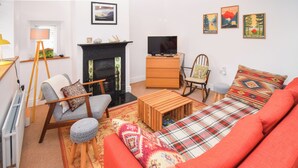 Een woonkamer met een bank, een televisie, een open haard en een raam met jaloezieën.