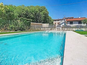Une piscine à l’eau d’un bleu limpide, entourée d’une zone pavée et, au fond, d’un bâtiment avec un toit rouge.