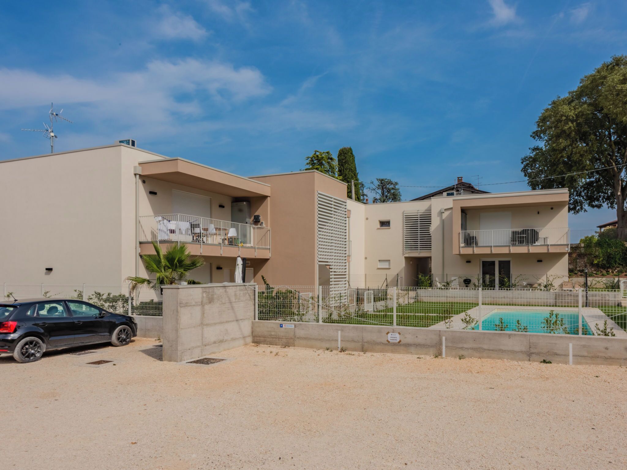 Un edificio residencial con piscina, un automóvil estacionado al frente y cielo despejado.