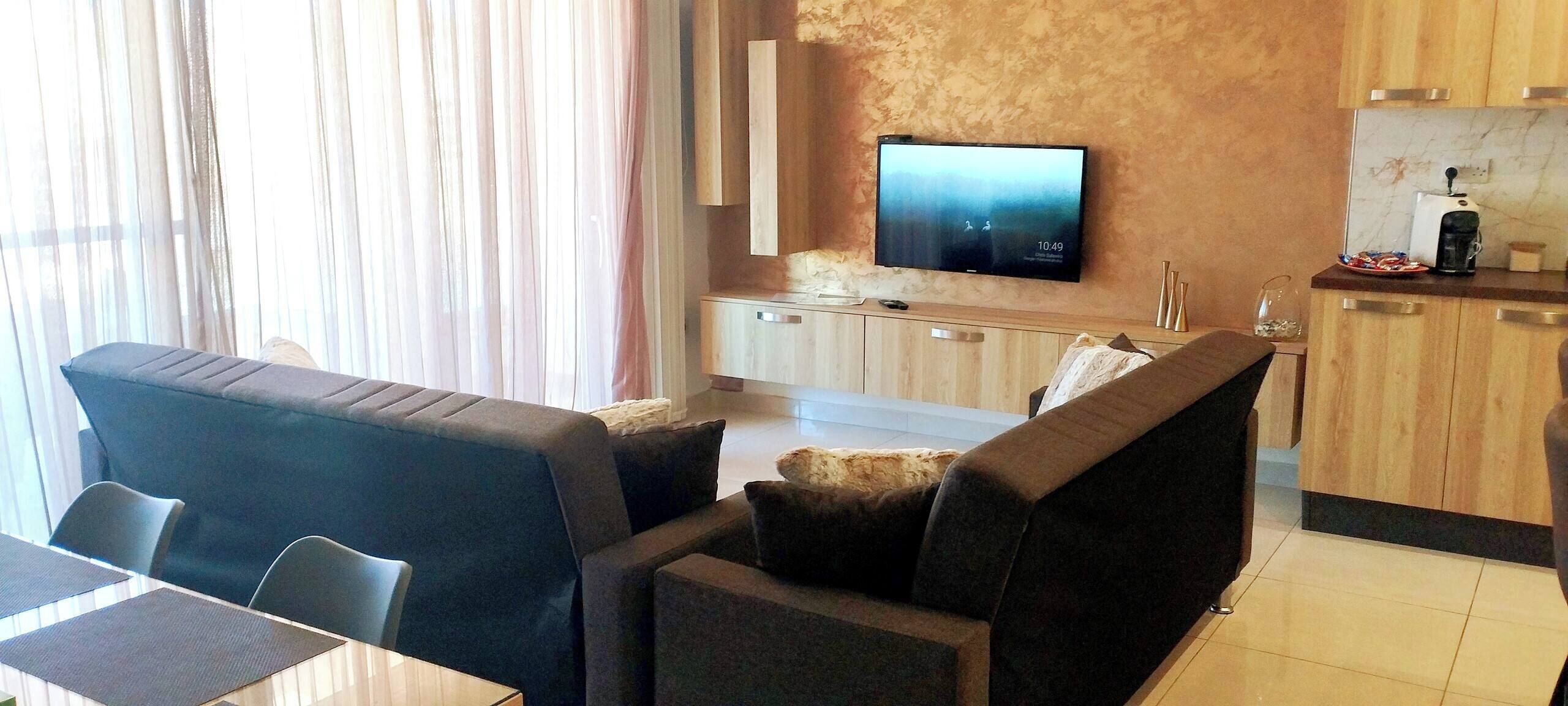 Un soggiorno moderno con una TV a schermo piatto, un divano, un tavolo da pranzo e un angolo cottura.