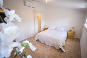 Une chambre à coucher comprenant un lit, des tables de chevet, une commode, un appareil de climatisation et une porte.