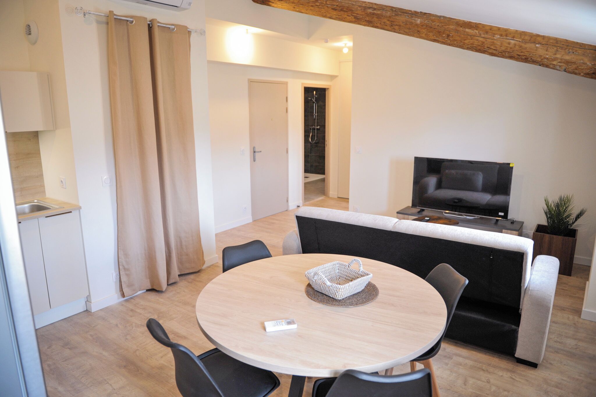 Een moderne woonkamer met een ronde eettafel, een grijze bank en een televisie.