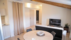 Een moderne woonkamer met een ronde eettafel, een grijze bank en een televisie.