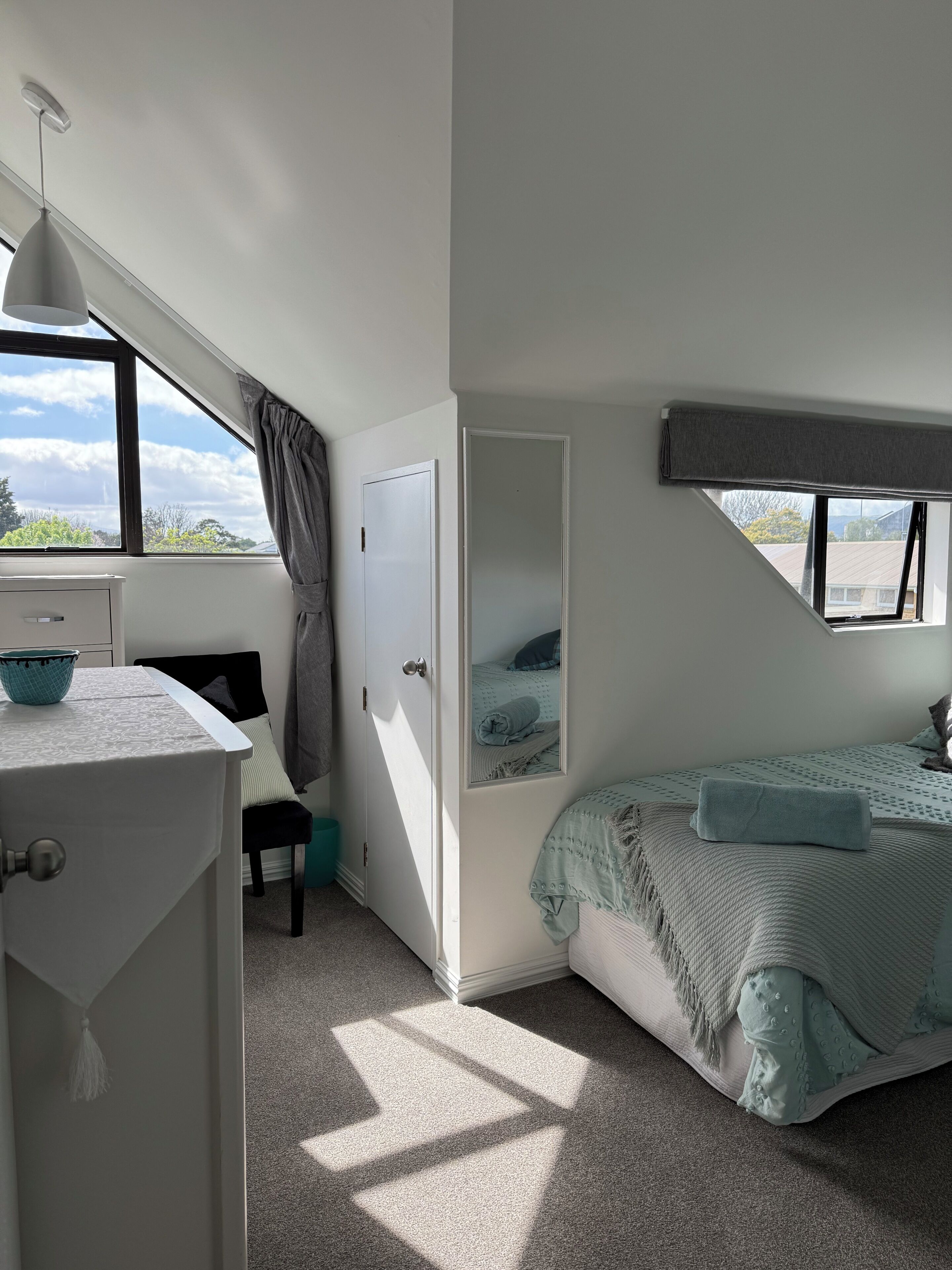 A bedroom with a bed, a desk, a chair, a window, and a door.