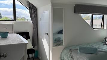 A bedroom with a bed, a desk, a chair, a window, and a door.