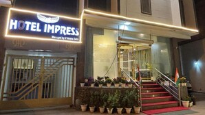 Entrada de hotel com uma placa indicando 'HOTEL IMPRESS', uma escadaria e plantas em vasos.