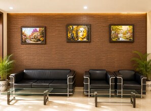 A lobby with two black leather sofas, a glass coffee table, and three framed paintings on a brick wall. - Hotel Impress by RMR Hotels (New Delhi)