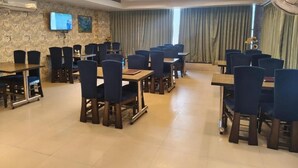 Uma sala de conferências com mesas, cadeiras, uma televisão e um amplo janelão com cortinas.