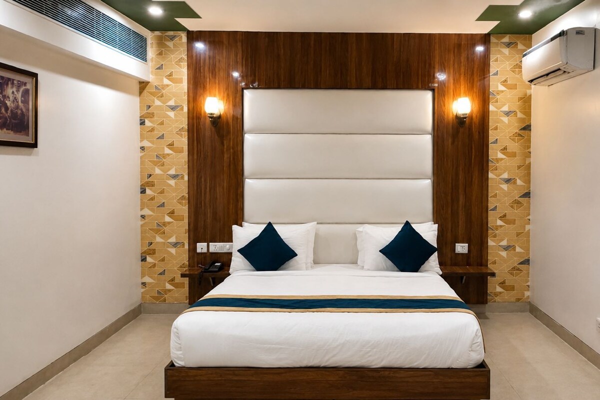 A hotel room with a large bed, wooden headboard, two bedside tables, a wall-mounted air conditioning unit, and a patterned wall.