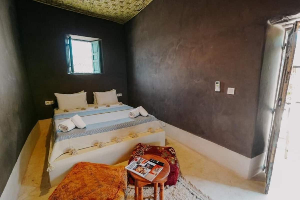 A bedroom with a bed, a small table, a window, and a door.