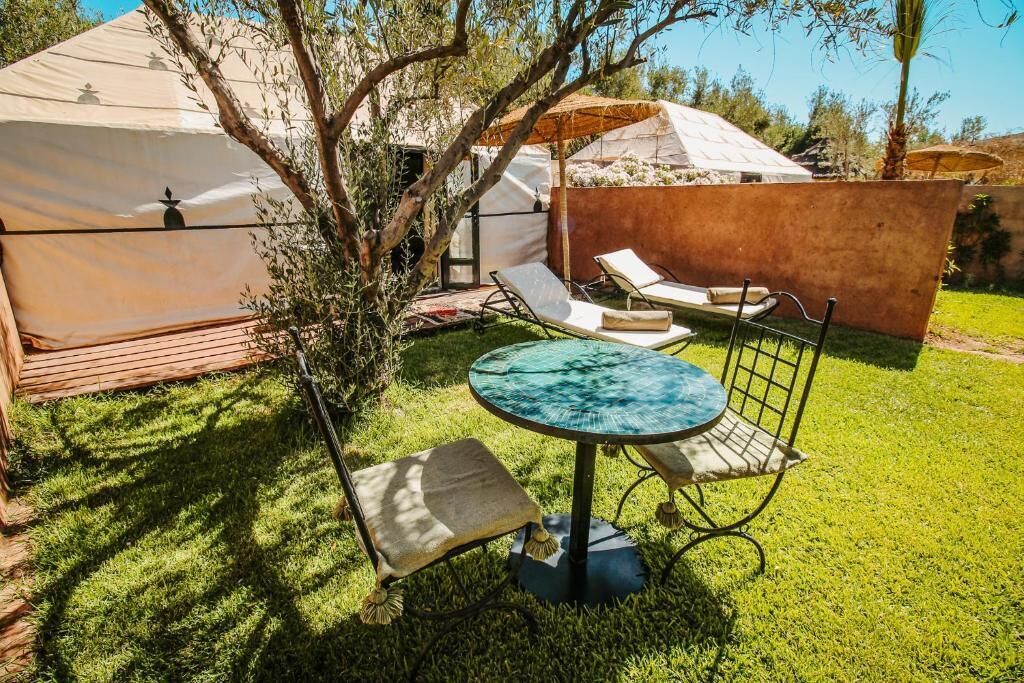 Un patio con una mesa redonda y dos sillones de descanso, rodeado por una terraza de madera y una carpa.