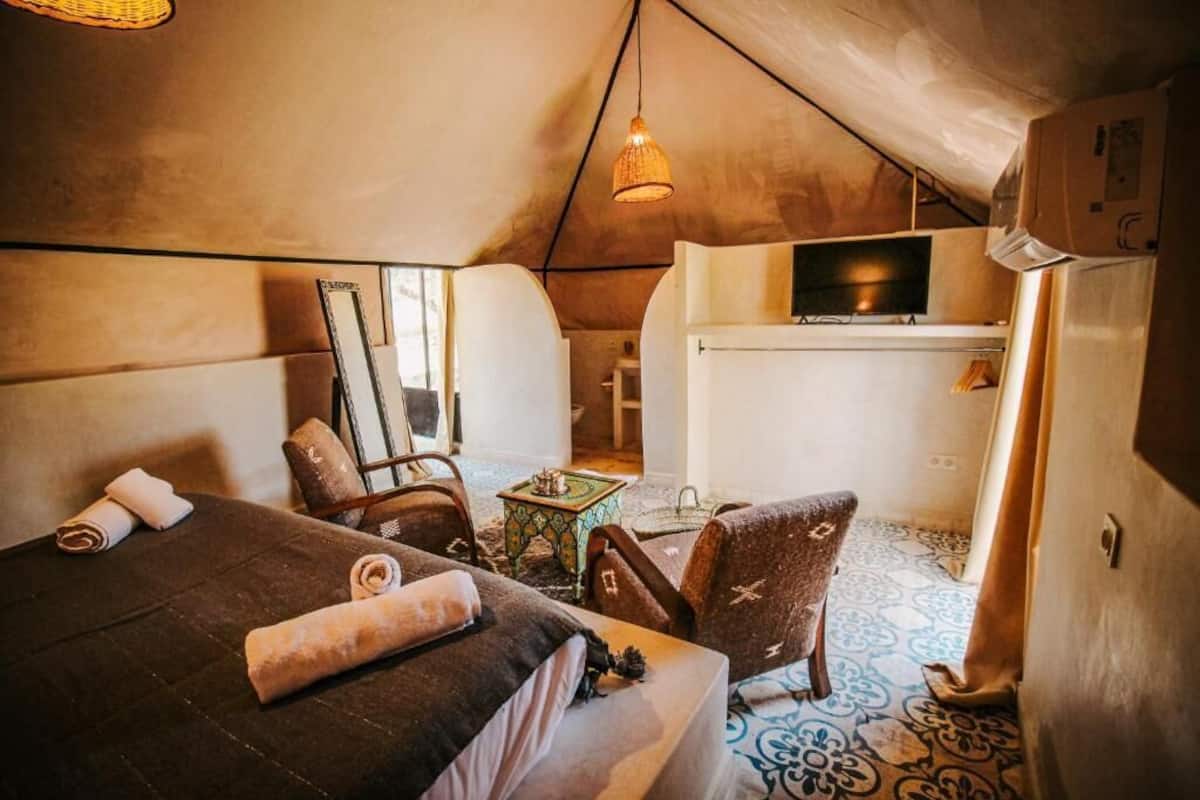 A cozy, tent-style room with a bed, chairs, a small table, and a television.