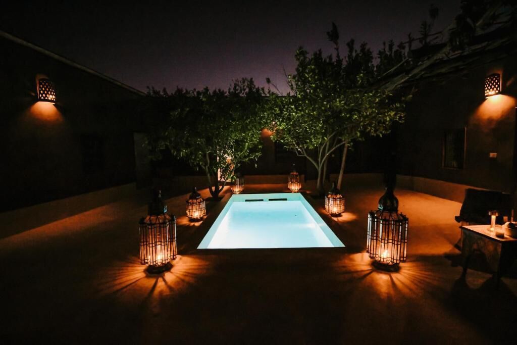 A pool area with a rectangular pool, surrounded by lanterns, and trees in the background.