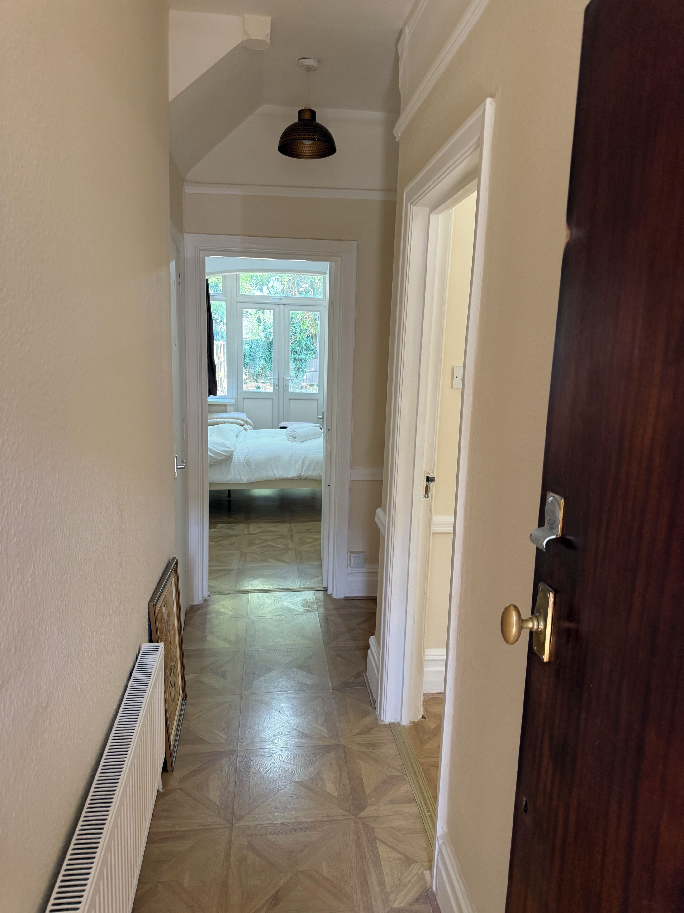 Un couloir avec un radiateur, une porte en bois et un lit à l’arrière-plan.