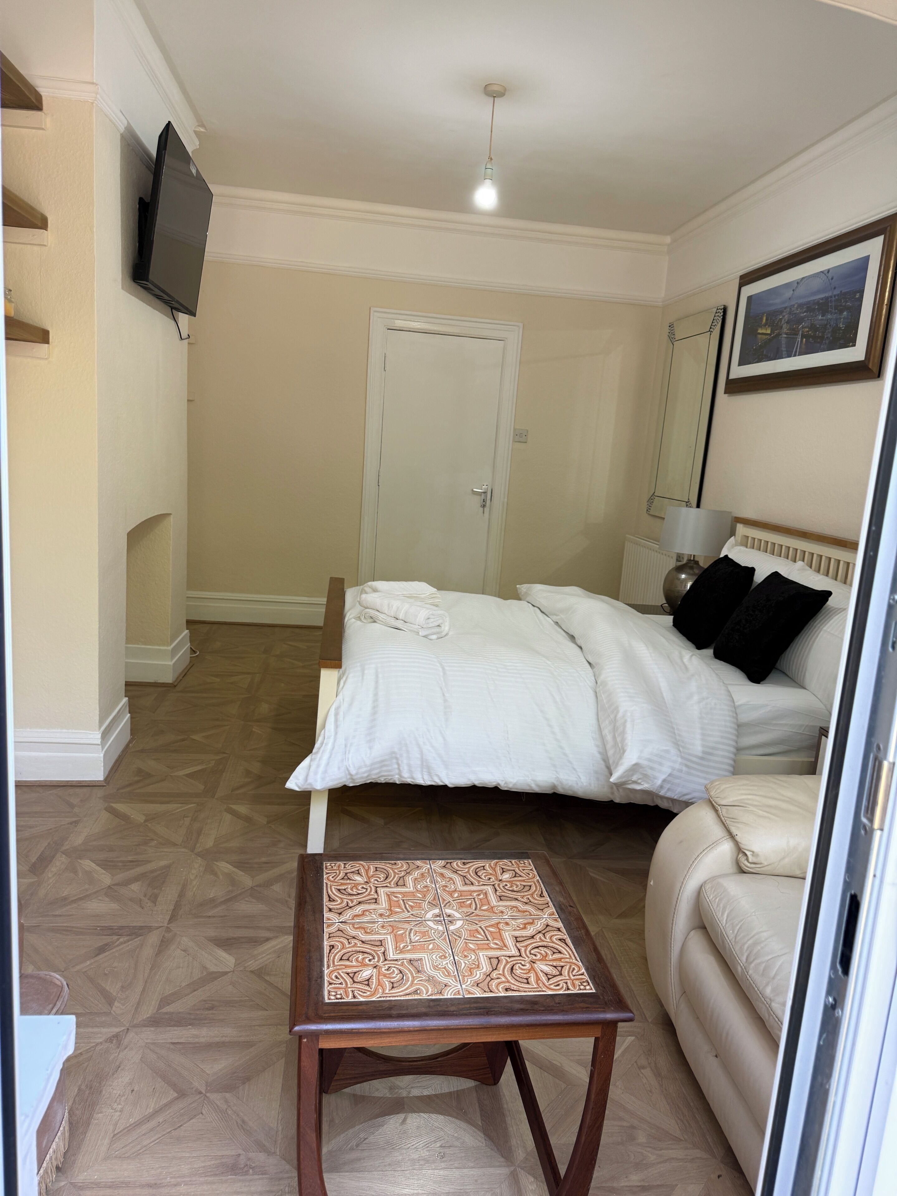A bedroom with a bed, a bedside table, a lamp, a chair, a television on the wall, and a door.