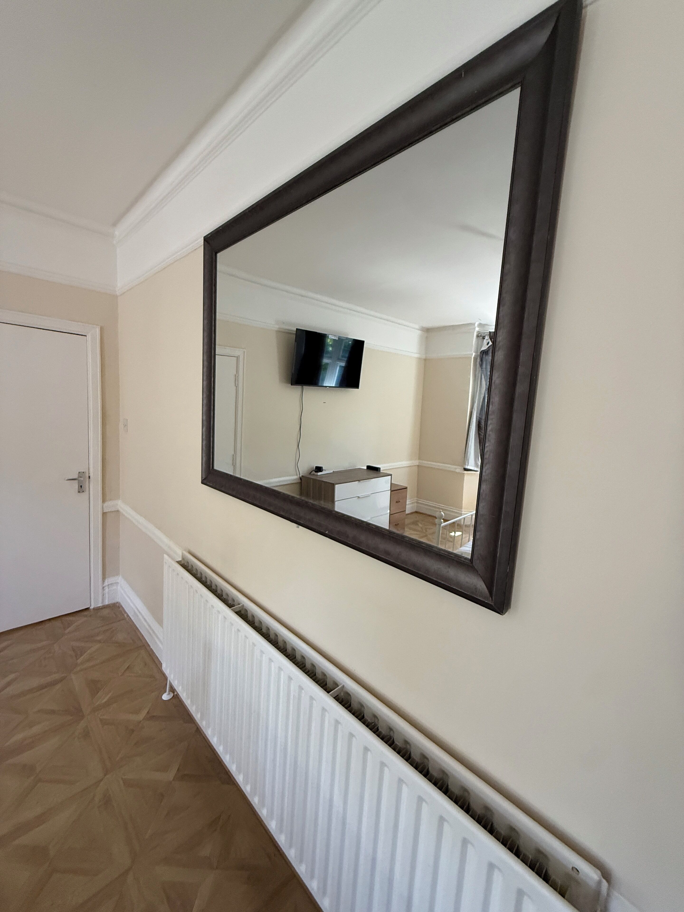 Un couloir avec un grand miroir, un radiateur et un téléviseur fixé au mur.