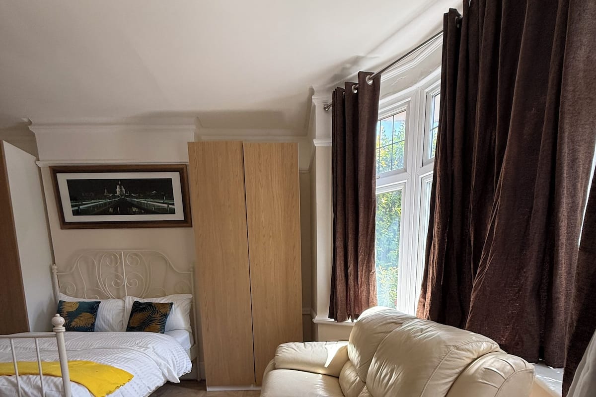 Quarto com cama, sofá, guarda-roupa e janela com cortinas.