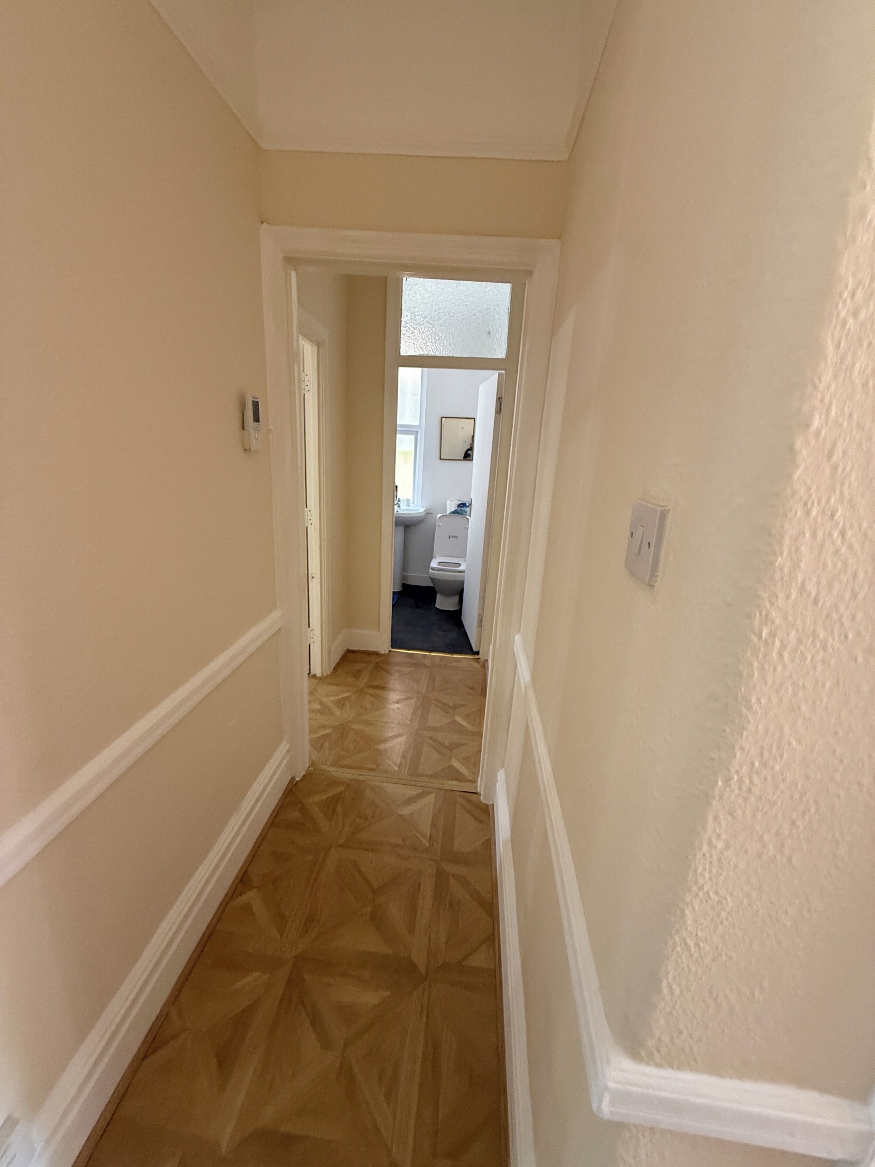 A hallway with a patterned floor, a door leading to a bathroom, and a light switch on the wall.