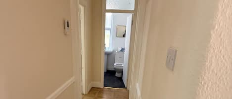 A hallway with a patterned floor, a door leading to a bathroom, and a light switch on the wall.