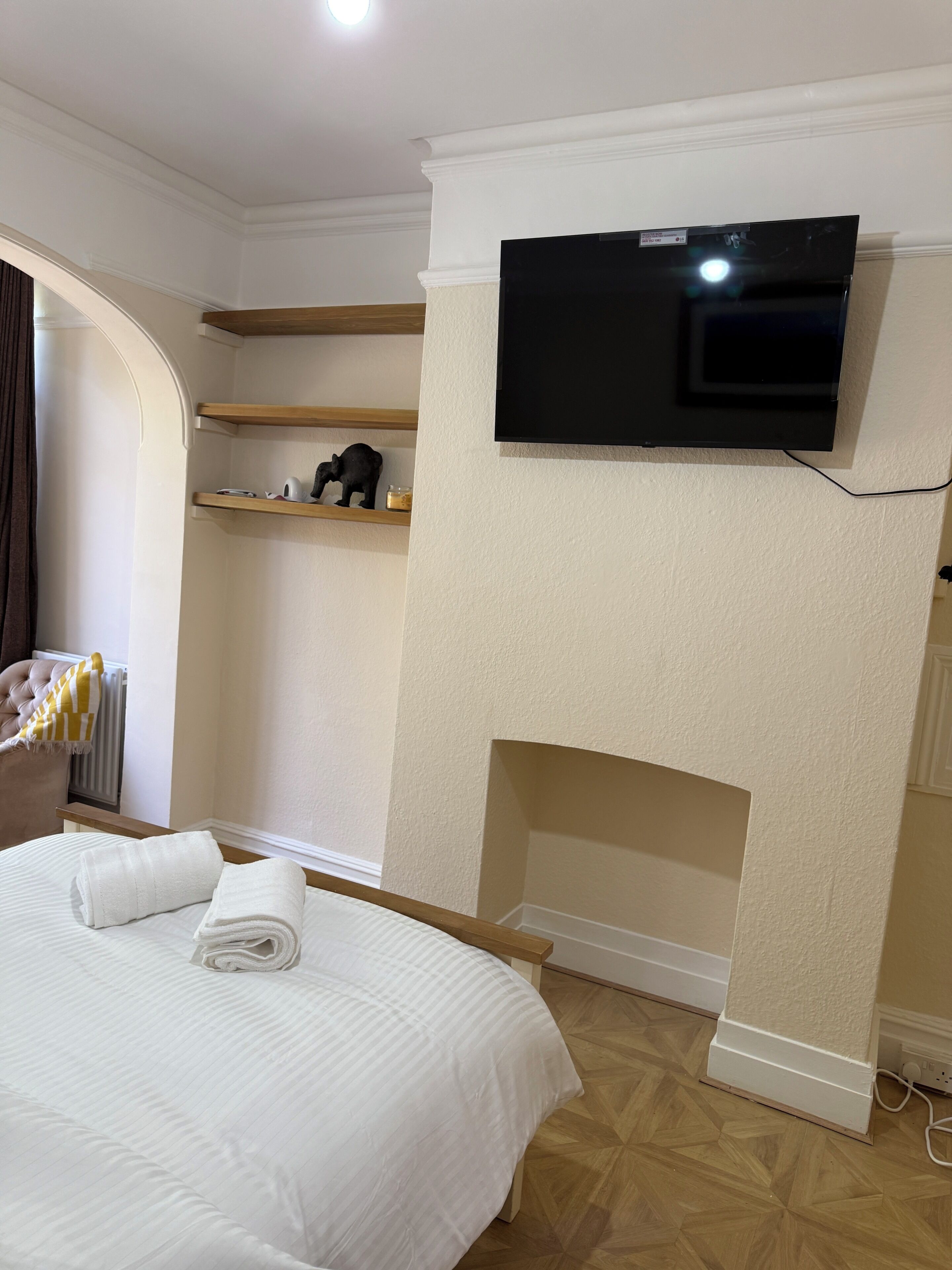 A hotel room with a bed, a television mounted on the wall, a fireplace, and wooden shelves.