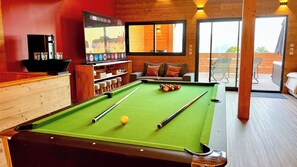 A pool table with balls, a television displaying a sports channel, and a seating area with a sofa and chairs.