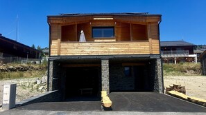 A two-story wooden cabin with a stone foundation, a covered entrance, and a small balcony on the upper floor.