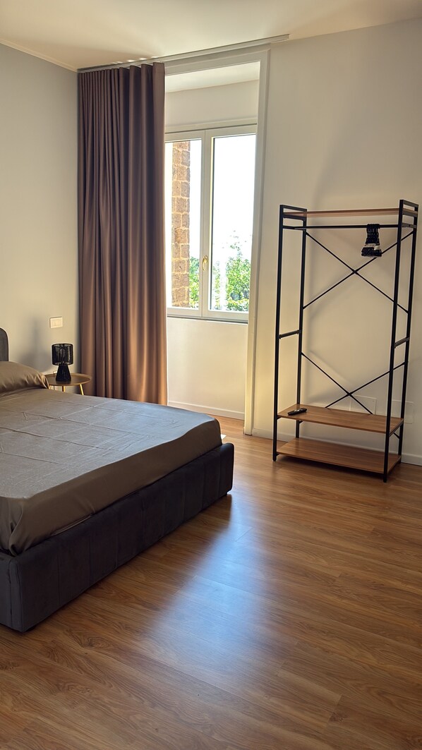 A bedroom with a bed, a bedside table with a lamp, a window with curtains, and a metal bed frame.