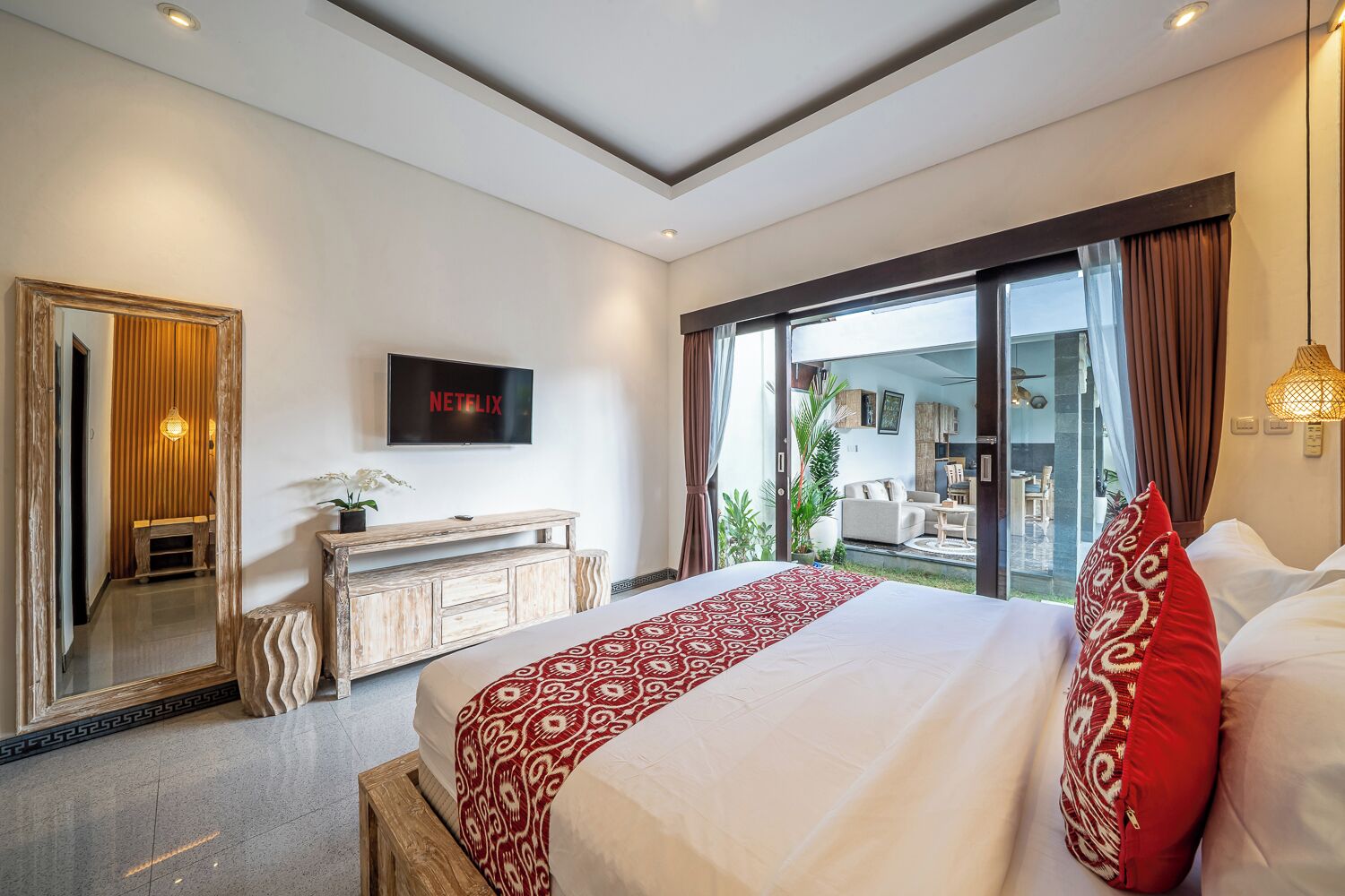A hotel room with a large bed, a TV mounted on the wall, a wooden dresser, and a sliding glass door leading to a balcony.