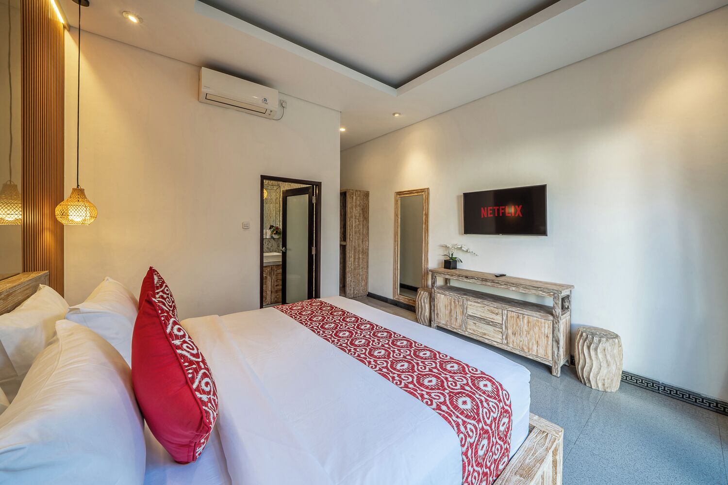 A modern hotel room with a bed, a TV, a dresser, and an air conditioning unit.