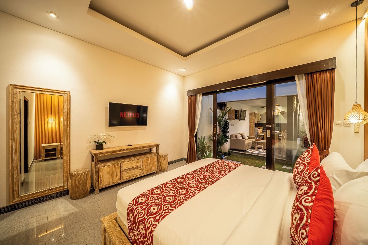 A modern hotel room with a large bed, a TV, a wooden console, a mirror, and a sliding glass door to the balcony.