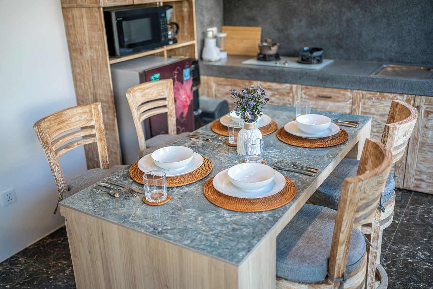 A dining table set with plates, bowls, cutlery, and a vase with flowers.