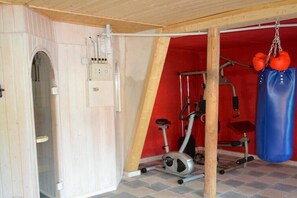 Ein Fitnessraum mit Trainingsgeräten, einem Boxsack und einer Tür zu einem weiteren Raum.