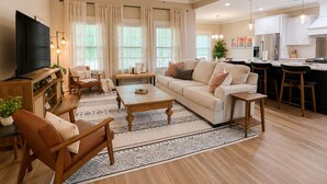 A modern living room with a sofa, coffee table, TV, and a kitchen area with bar stools.