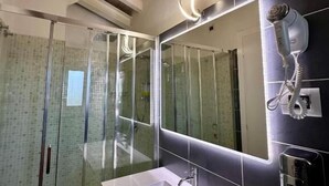 A modern bathroom with a large mirror, a built-in hairdryer, and a glass shower enclosure.