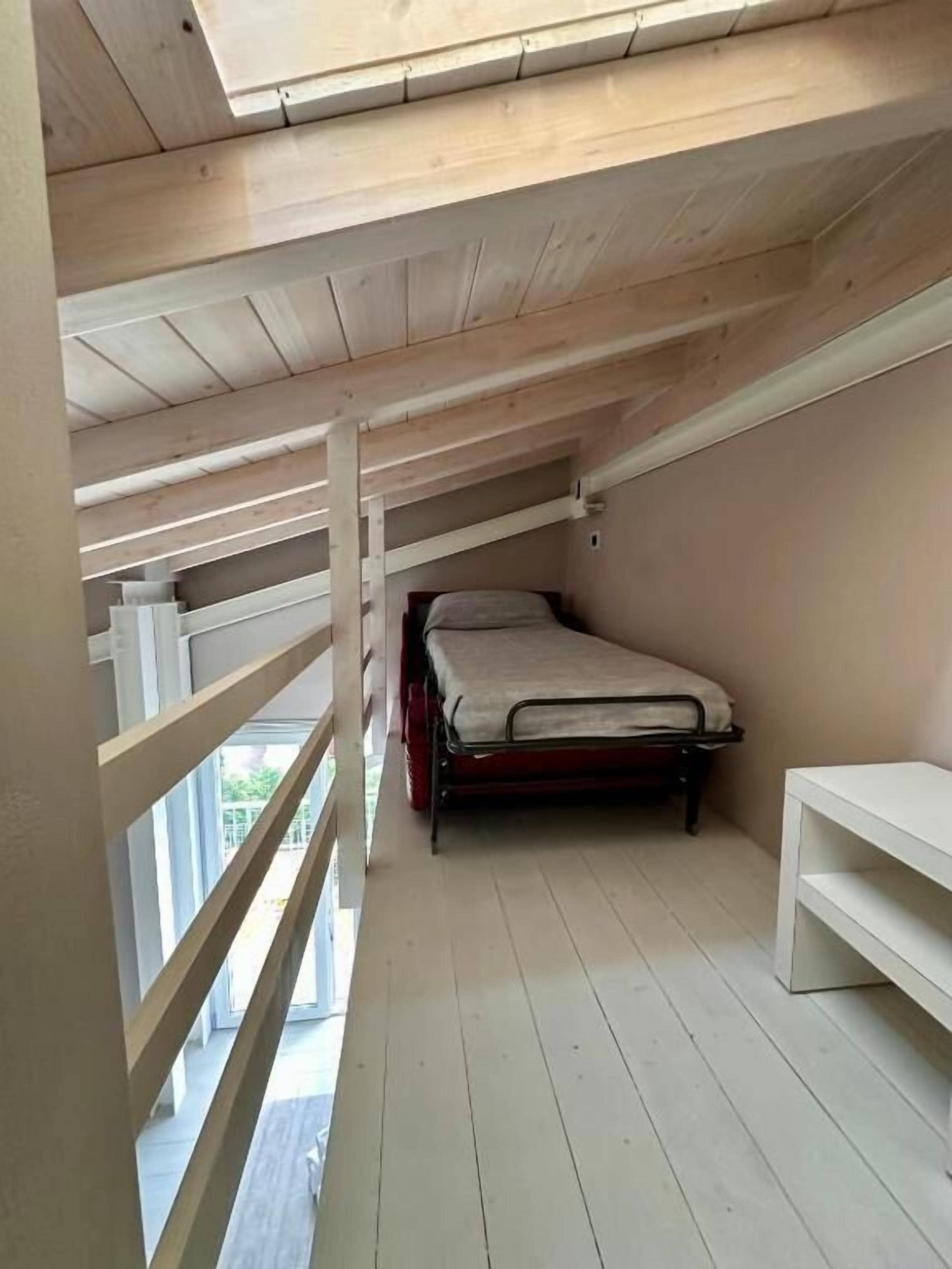 A small attic bedroom with a bunk bed, a white bench, and a skylight.