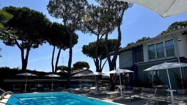 A swimming pool with lounge chairs and umbrellas, surrounded by trees and a building.