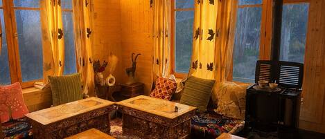 A cozy cabin with wooden walls, a fireplace, and a large window with curtains.
