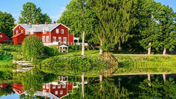 A red house with a white fence, a pond, and trees. - Husby Wardshus (Dala-Husby)