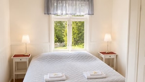 A neatly arranged bedroom with a large bed, two bedside tables with lamps, a window with a view of greenery, and a door on the right. - Husby Wardshus (Dala-Husby)