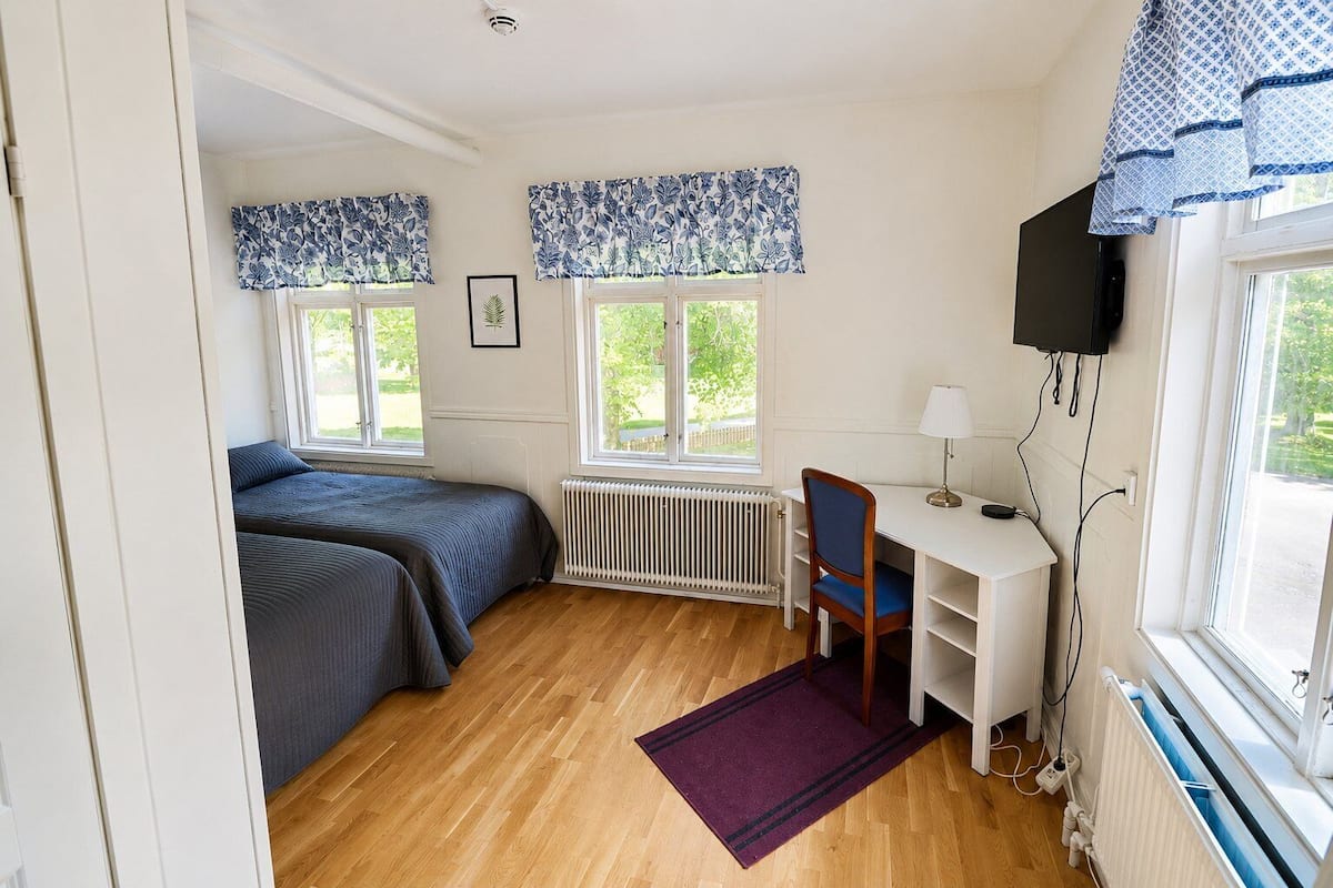 A room with two beds, a desk, a chair, a radiator, and a TV.