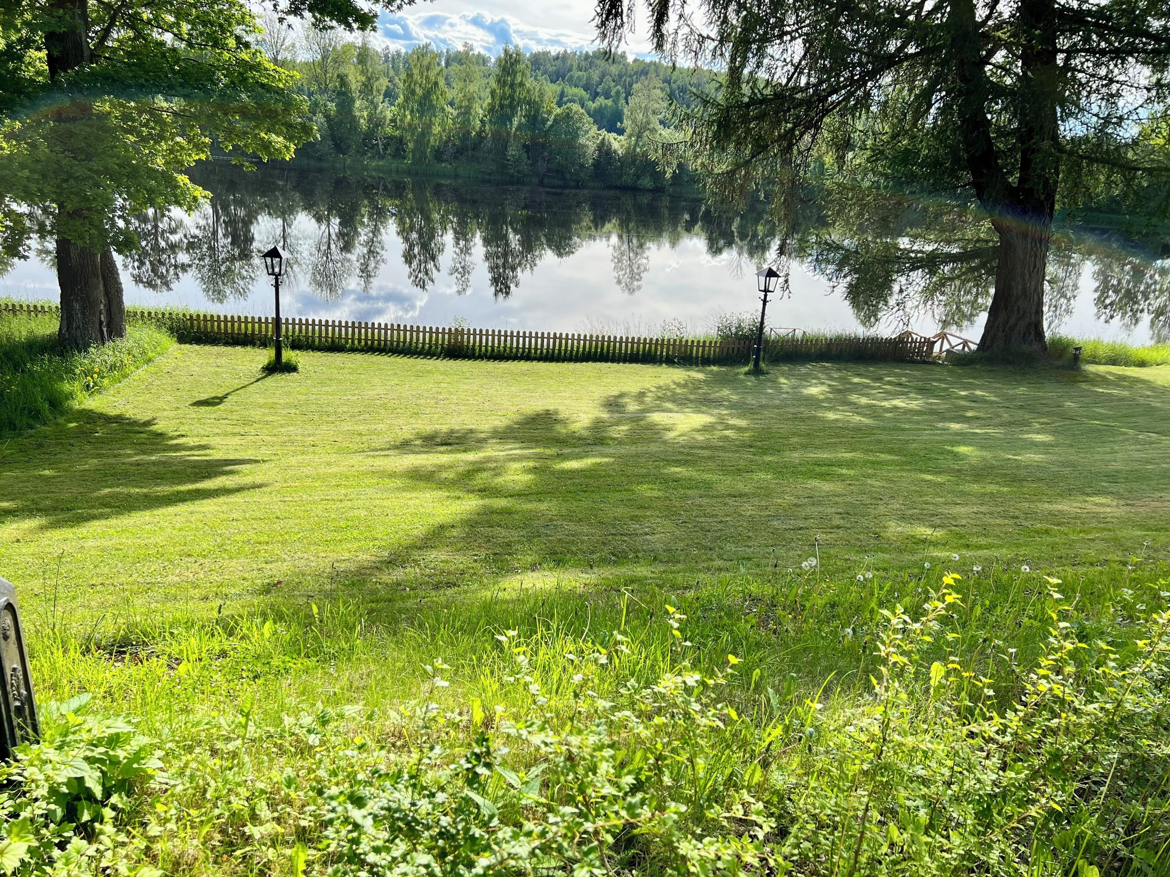 Un parque tranquilo junto al lago, con valla de madera, faroles y abundante vegetación.