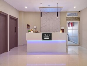 A reception desk with a sign indicating it's company-serviced, a potted plant, a small statue, and a window above the door. - Classic Cloud Stay (Guwahati)