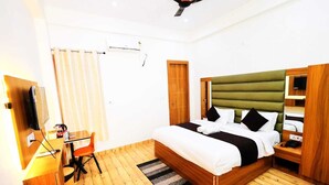 Una habitació d'hotel amb terra de fusta, un llit amb capçalera tapissada de color verd, un escriptori amb una cadira, una televisió i un armari de fusta.