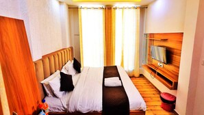 Habitació d'hotel amb llit, cortines, televisió i terra de fusta.