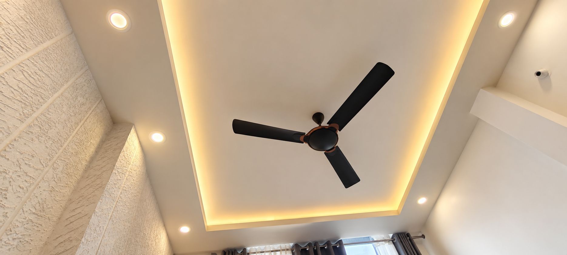 A ceiling fan with a light fixture and recessed lighting in a room with a textured wall.