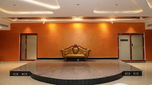 A lobby with a central stage, two doors, and a sofa. - G Grand Inn (Thanjavur)
