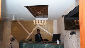 A hotel reception area with a marble counter, a ceiling fan, and a TV mounted on the wall. - G Grand Inn (Thanjavur)
