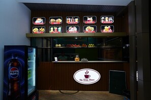 A food kiosk with a Pepsi refrigerator and a menu board displaying items like tea, coffee, snacks, and fresh juice.