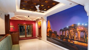 A hotel lobby with a reception desk, seating area, and a mural of a temple. - G Grand Inn (Thanjavur)