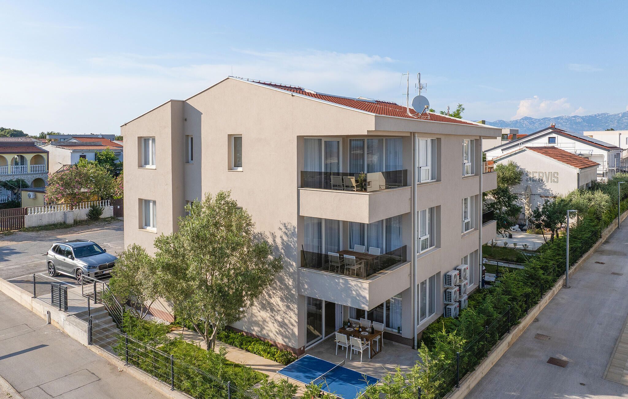 A multi-story building with balconies, a swimming pool, and a car parked in front.